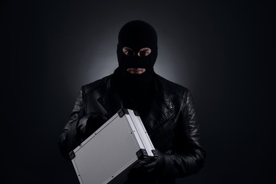 Photo of Man wearing knitted balaclava with metal briefcase on black background