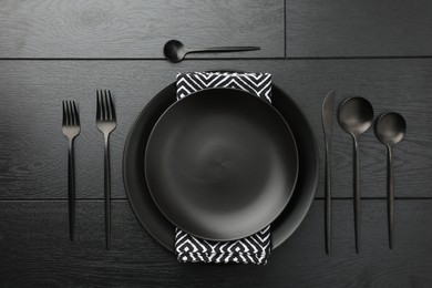 Stylish setting with cutlery and plates on black wooden table, flat lay