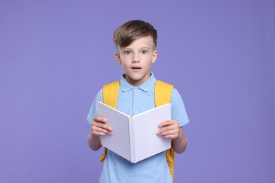 Photo of Cute schoolboy with book on violet background