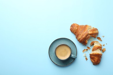 Photo of Delicious fresh croissant and cup of coffee on light blue background, flat lay. Space for text
