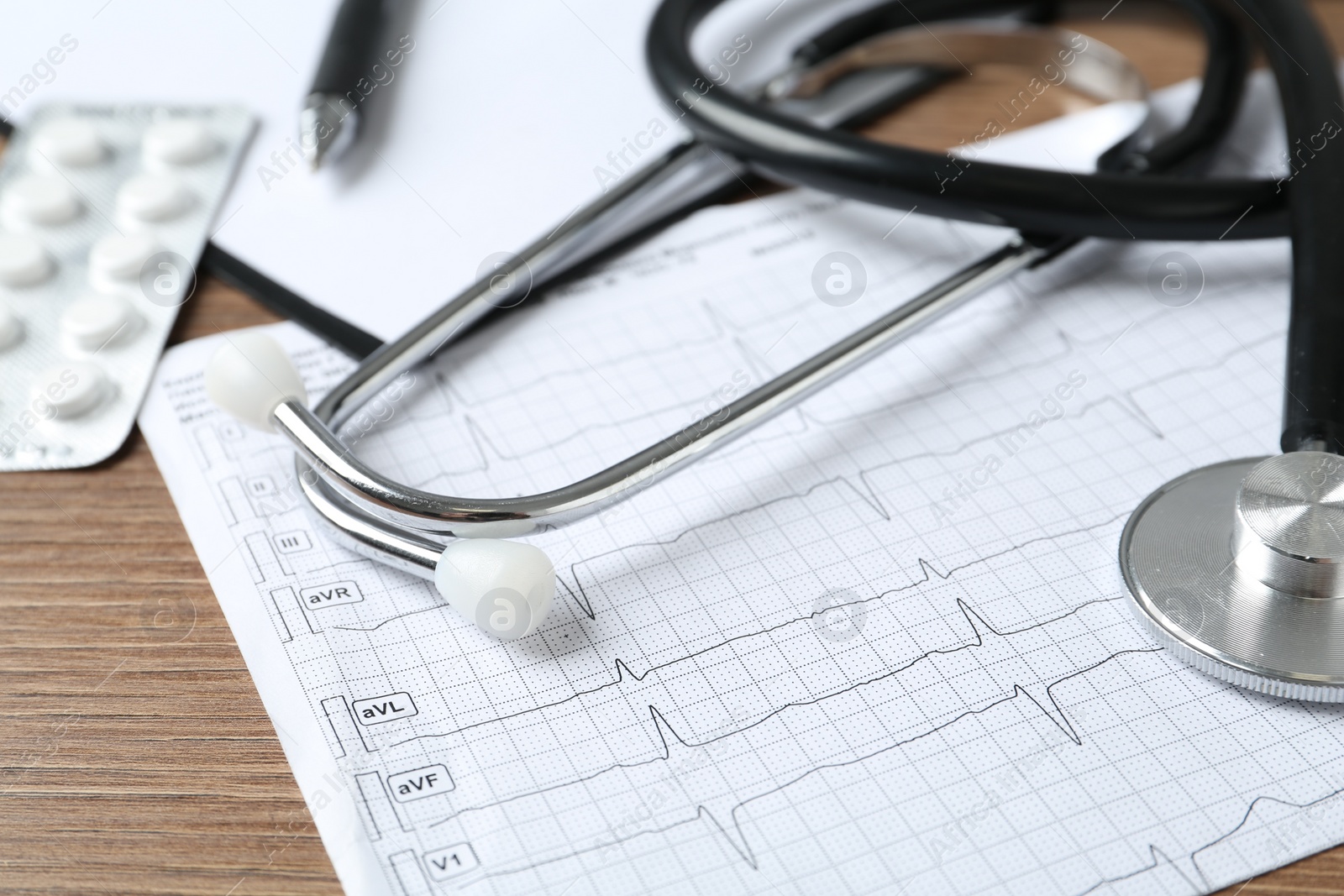 Photo of Cardiogram report, stethoscope and pills on wooden table, closeup