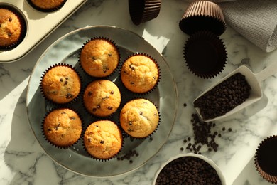 Photo of Delicious sweet muffins with chocolate chips on white marble table, flat lay