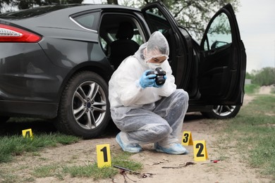 Photo of Criminologist in protective suit taking photo of evidences at crime scene outdoors