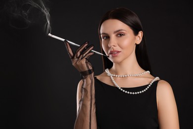 Woman using long cigarette holder for smoking on black background, space for text