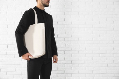 Young man holding textile bag against brick wall, closeup.  Mockup for design