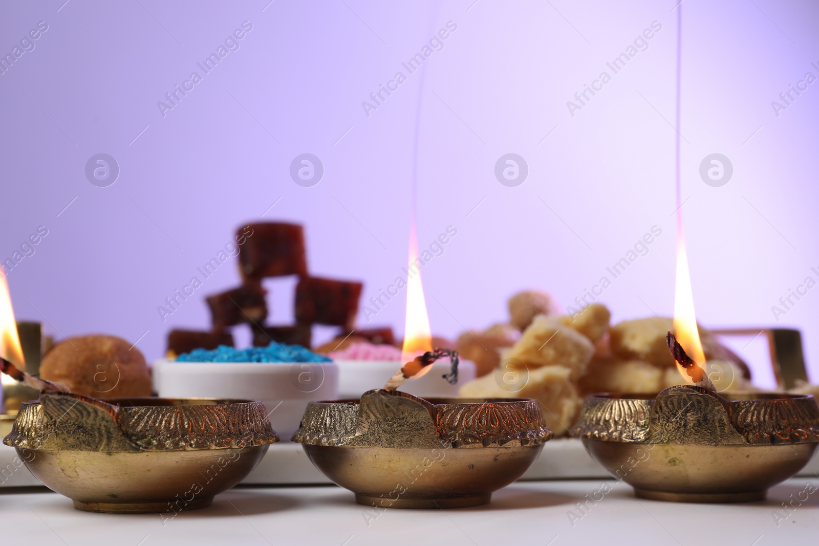 Photo of Happy Diwali. Diya lamps on white table against violet background, closeup