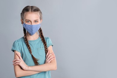 Photo of Girl wearing protective mask on grey background, space for text. Child's safety from virus