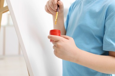 Photo of Little boy painting in studio, closeup. Using easel to hold canvas