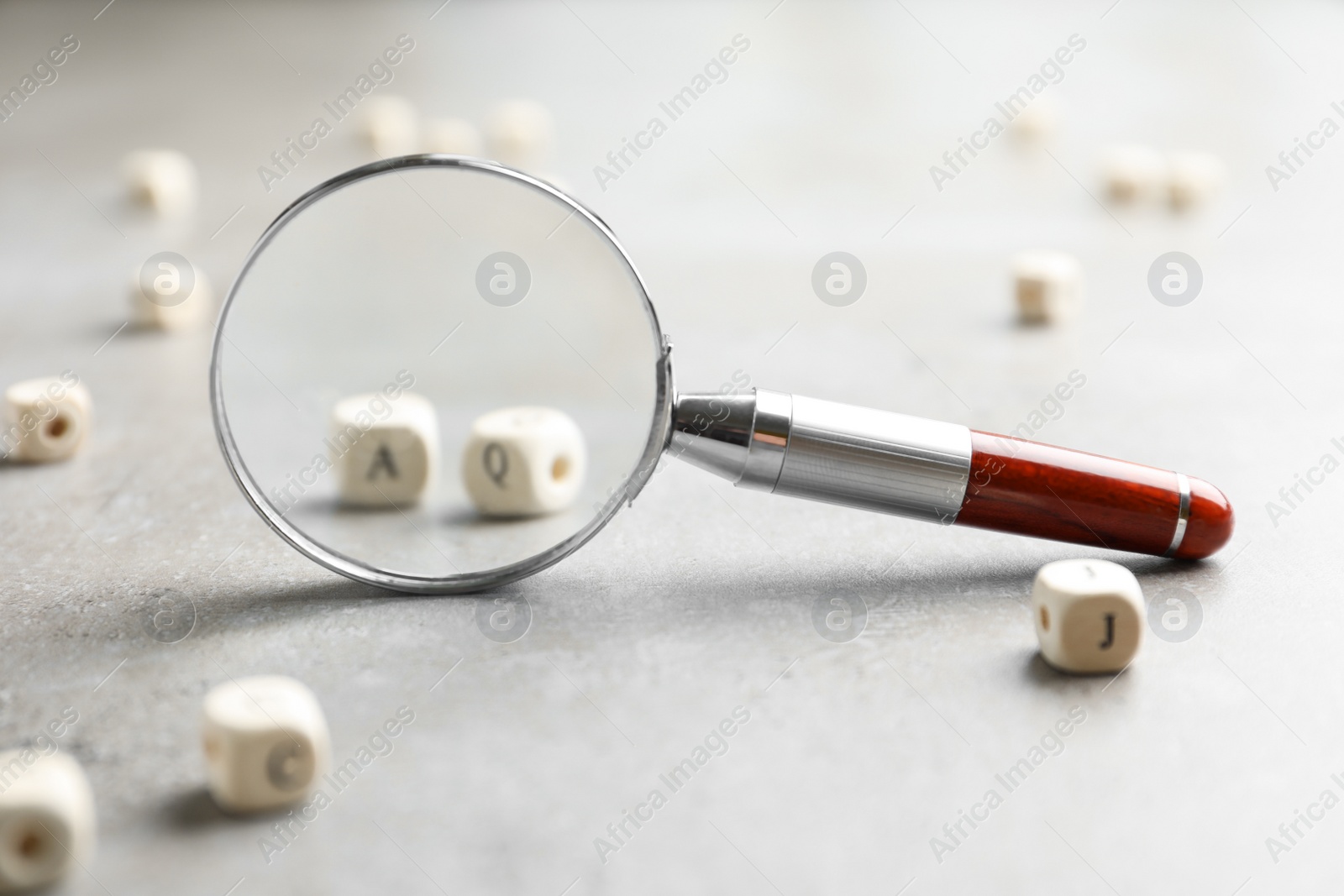 Photo of View on cubes with letters A and Q through magnifying glass at light grey stone background, closeup. Find keywords concept