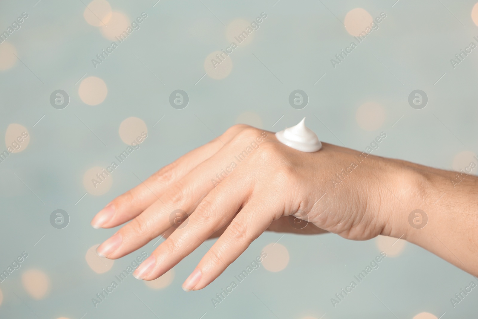 Photo of Woman applying hand cream on blurred background, closeup