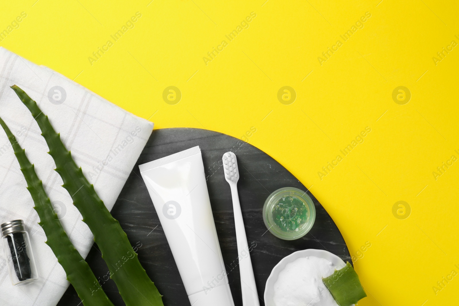 Photo of Aloe vera toothpaste in blank tube, brush, green leaves and care products on yellow background, top view. Space for text