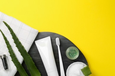 Aloe vera toothpaste in blank tube, brush, green leaves and care products on yellow background, top view. Space for text