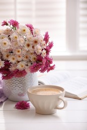 Photo of Cup of fresh coffee, open book and beautiful bouquet on white wooden table near window. Good morning