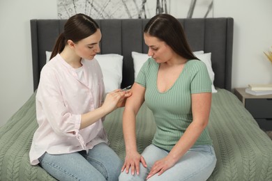 Woman giving insulin injection to her diabetic friend in bedroom