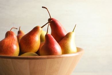 Bowl with ripe pears on light background, closeup