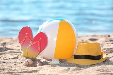 Photo of Inflatable ball, hat and flip flops on sand near sea. Beach object