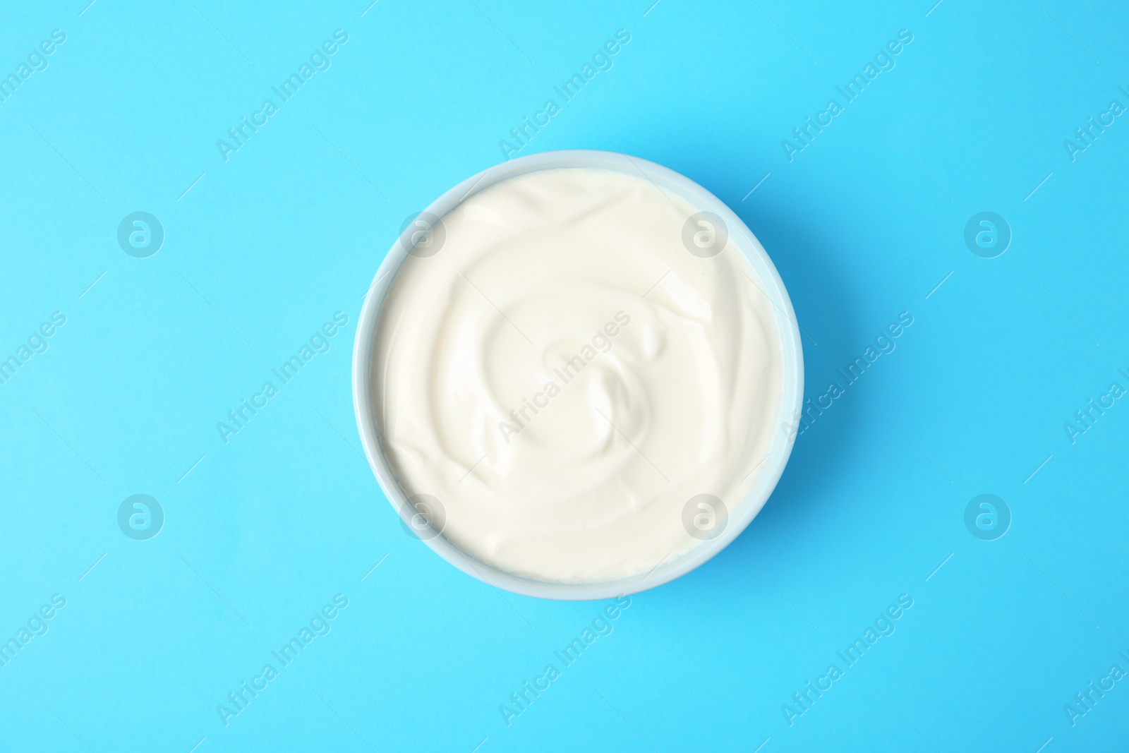 Photo of Bowl of sour cream on light blue background, top view