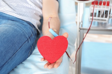 Photo of Man holding heart while making blood donation at hospital, closeup