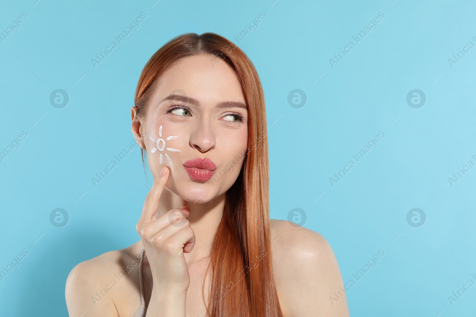 Photo of Beautiful young woman with sun protection cream on her face on light blue background, space for text