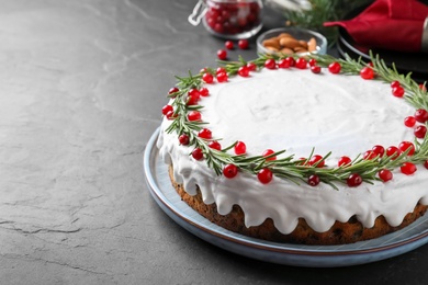 Traditional Christmas cake decorated with rosemary and cranberries on dark grey table, space for text