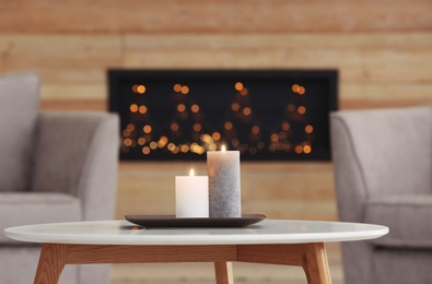 Plate with burning candles on table in living room