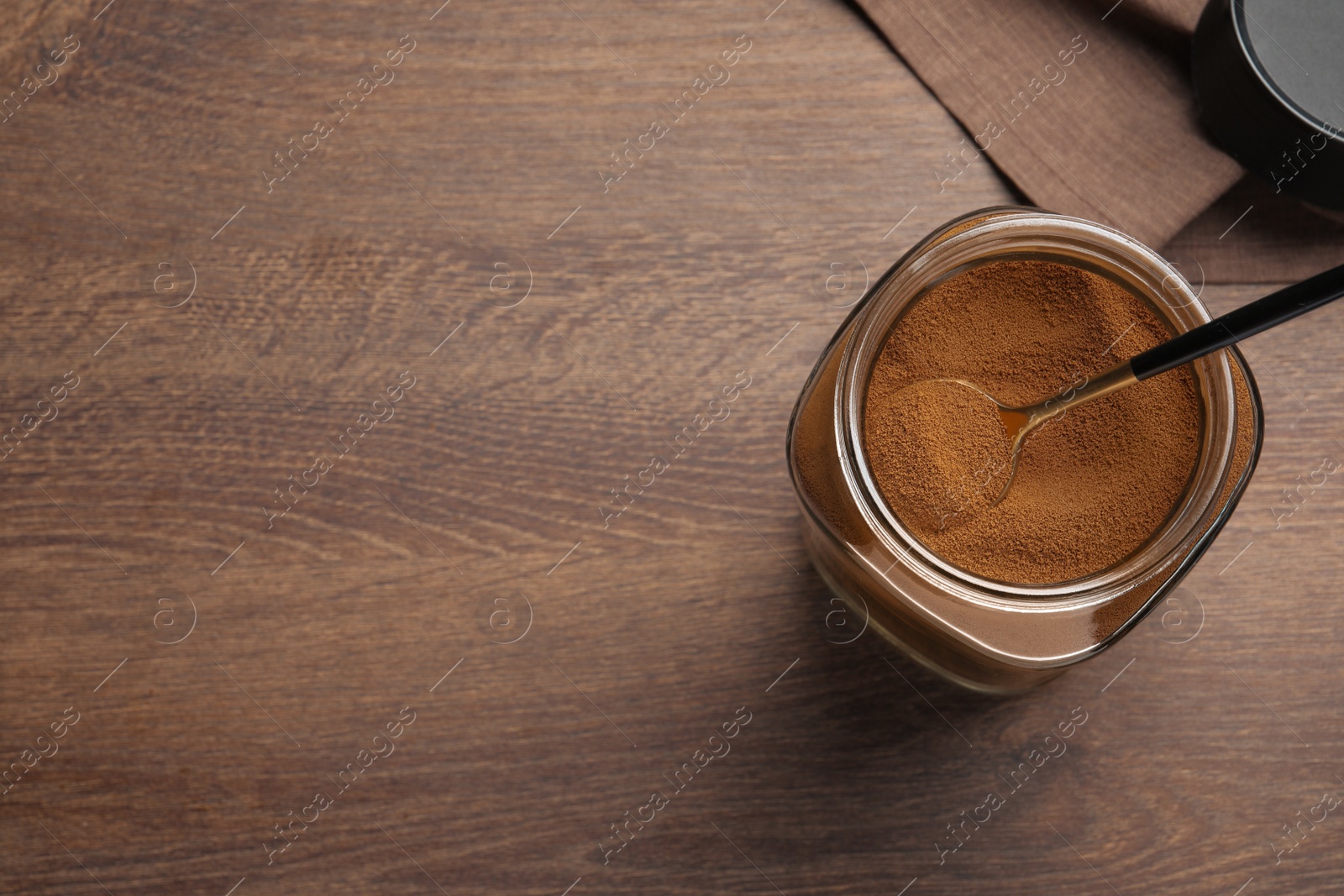 Photo of Jar of instant coffee and spoon on wooden table, top view. Space for text