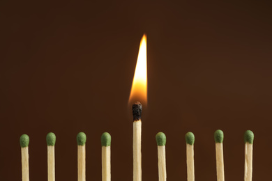 Photo of Burning match among unlit ones on brown background, closeup