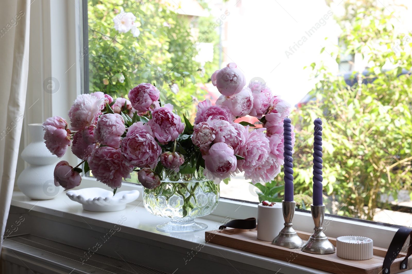 Photo of Beautiful pink peonies in vase and tray with candles on window sill. Interior design