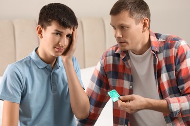 Photo of Father giving condom to his teenage son in bedroom. Sex education concept