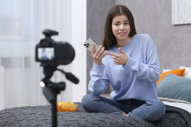 Photo of Smiling teenage blogger pointing at smartphone while streaming at home