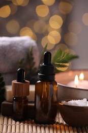 Photo of Spa composition. Bottles of essential oil and sea salt in bowl on table against blurred lights, closeup
