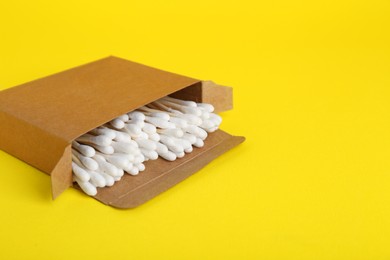 Photo of Box with wooden cotton buds on yellow background. Space for text