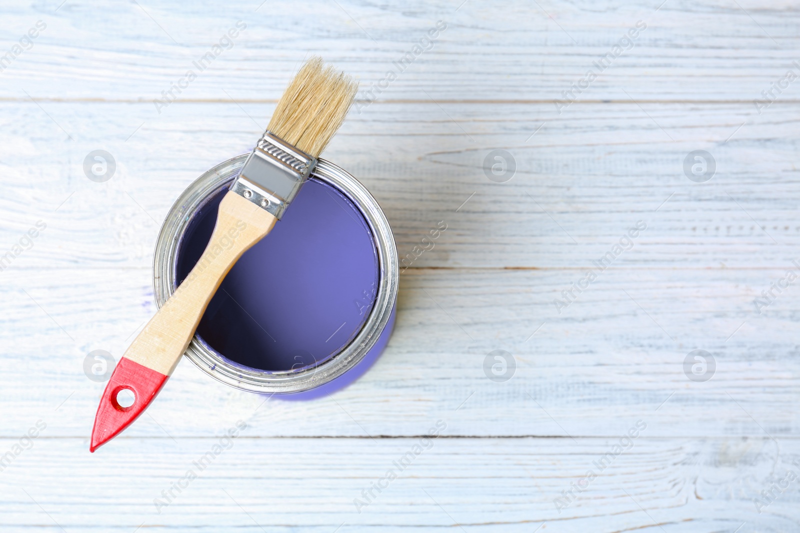 Image of Tin can with violet paint and brush on white wooden background, top view. Space for text