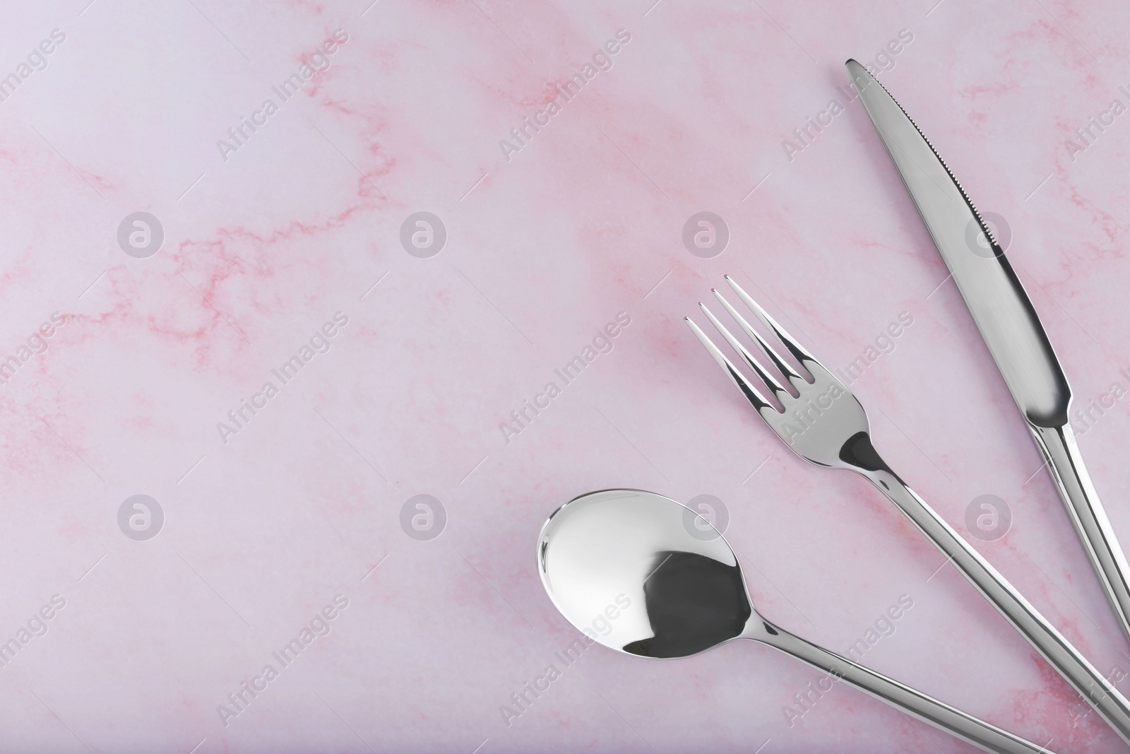 Photo of Stylish cutlery set on pink marble table, flat lay. Space for text