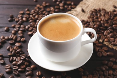 Cup of hot aromatic coffee and roasted beans on wooden table