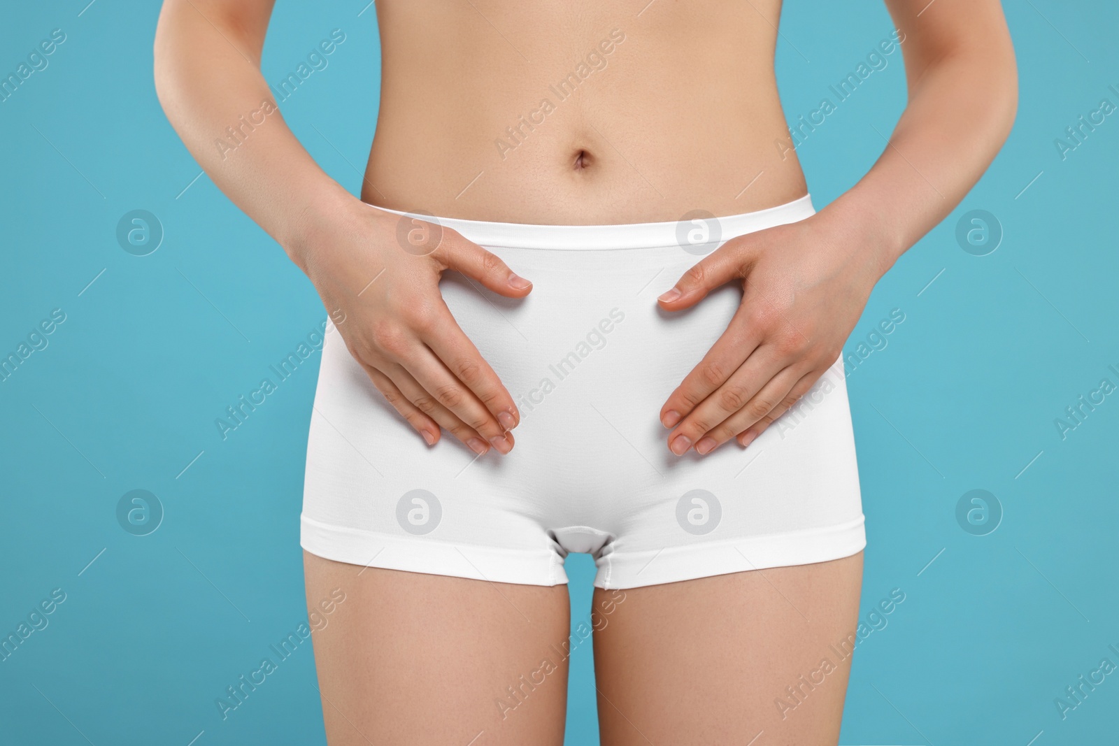 Photo of Woman holding hands near panties on light blue background, closeup. Women's health