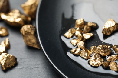 Plate with gold nuggets on black table, closeup