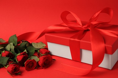 Beautiful gift box with bow and roses on red background