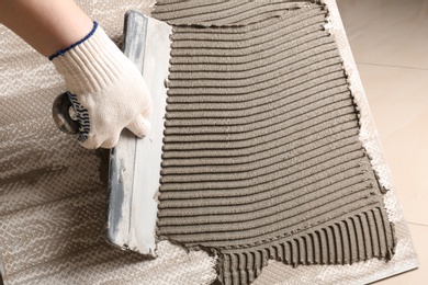 Photo of Worker spreading concrete on ceramic tile with spatula, closeup. Space for text