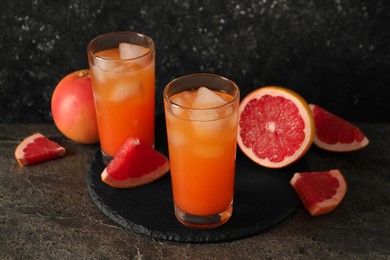 Photo of Tasty grapefruit drink with ice in glasses and fresh fruits on dark textured table
