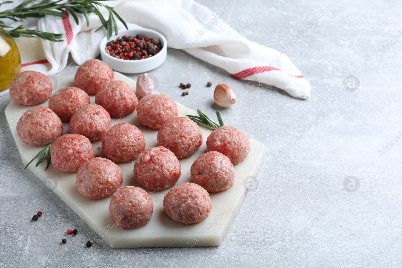 Photo of Many fresh raw meatballs and ingredients on light grey table, space for text