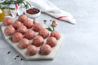 Photo of Many fresh raw meatballs and ingredients on light grey table, space for text