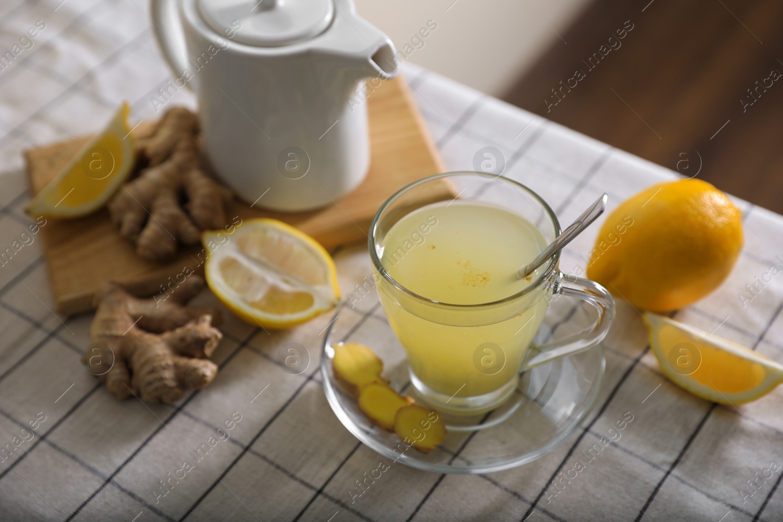 Photo of Glass of aromatic ginger tea and ingredients on white checkered tablecloth indoors, space for text