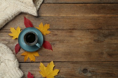 Photo of Cup of hot coffee, sweater and autumn leaves on wooden table, flat lay. Space for text