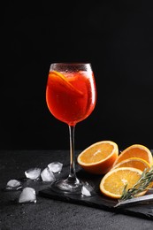 Photo of Glass of tasty Aperol spritz cocktail with orange slices and ice cubes on table against black background