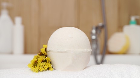 Photo of Towel with bath bomb and flowers on tub indoors, closeup