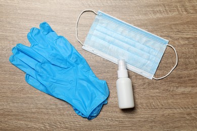 Photo of Medical gloves, mask and hand sanitizer on wooden background, flat lay. Safety equipment