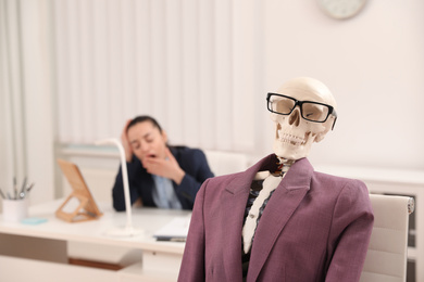 Human skeleton with suit and glasses in office. Space for text