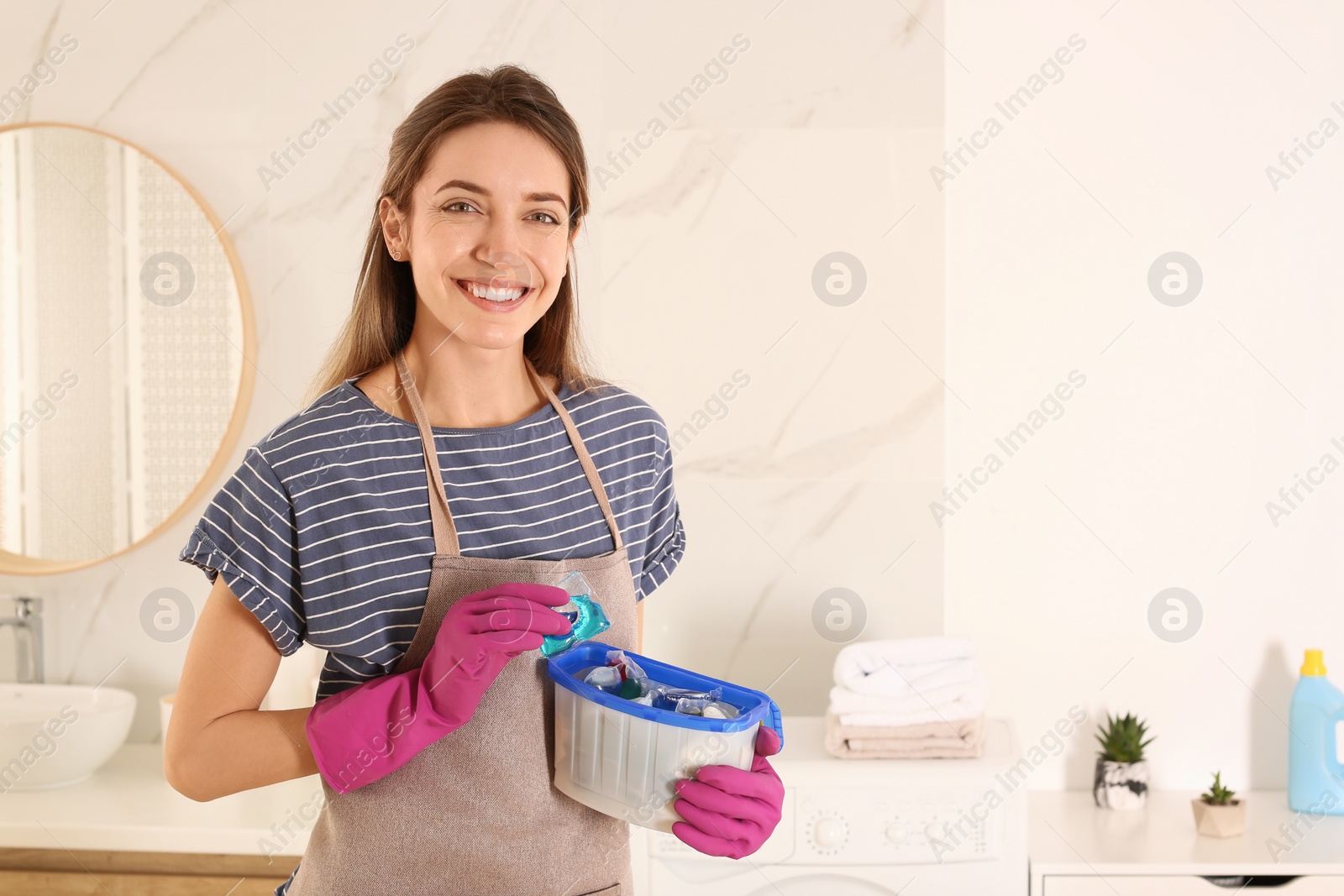 Photo of Woman holding container with laundry detergent capsules in bathroom