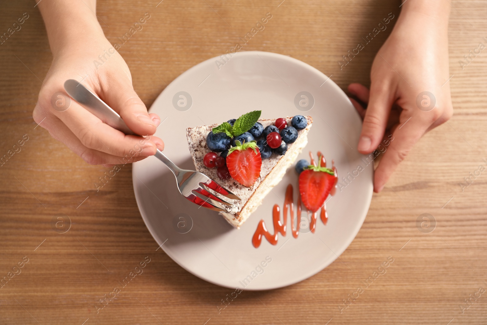 Photo of Woman eating delicious homemade cake with fresh berries at table, top view